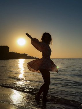 Kumsalda dans eden genç bir kadının silueti. Yaz tatilleri konsepti
