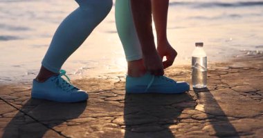 Yaz antrenmanından önce spor ayakkabılarına ayakkabı bağlayan kadın koşucunun yakın çekimi. Fitness ve sağlıklı yaşam tarzı konsepti, açık hava koşusuna hazırlanma ve sağlıklı aktif rutin. Yavaş çekim