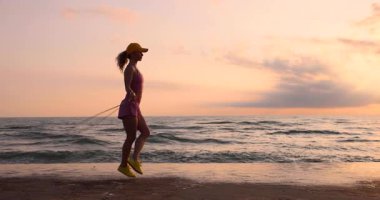 Sahilde ip atlayan genç bir kadın. Sporcu kadın denizlere ve gökyüzüne karşı. Yaz sporu ve sağlıklı yaşam tarzı konsepti