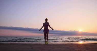 Sahilde ip atlayan genç bir kadın. Sporcu kadın denizlere ve gökyüzüne karşı. Yaz sporu ve sağlıklı yaşam tarzı konsepti