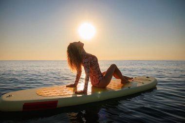 Denizin kıyısında ayakta duran kürek çeken mutlu bir kadın. Yaz tatili boyunca gün doğumunda eğlenen bir kadın. Sağlıklı yaşam tarzı kavramı