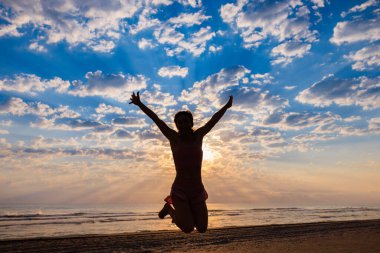Sahilde güneşin doğuşunun keyfini çıkaran zinde bir kadın. Denize ve gökyüzüne karşı atlayan genç bir kadın. Yaz sporu ve sağlıklı yaşam tarzı konsepti