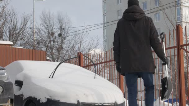 Un hombre limpia un coche de nieve — Vídeos de Stock