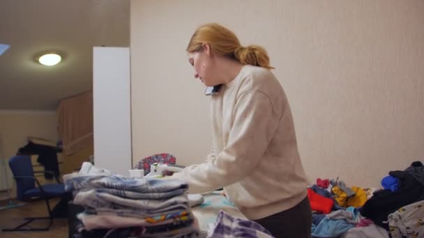 Mujer dobla la ropa y hablando por teléfono — Vídeos de Stock