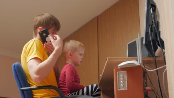 Человек с телефоном за компьютером с сыном — стоковое видео