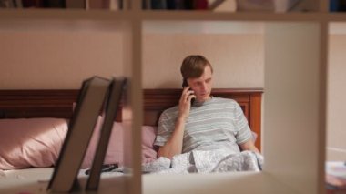 Yatakta adam telefonda konuşuyor.