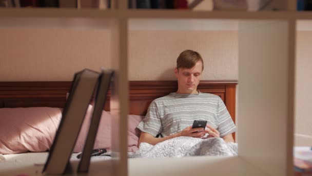 Unge man på sängen med smartphone — Stockvideo