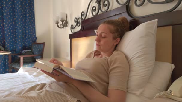 Egy nő könyvet olvas az ágyról — Stock videók