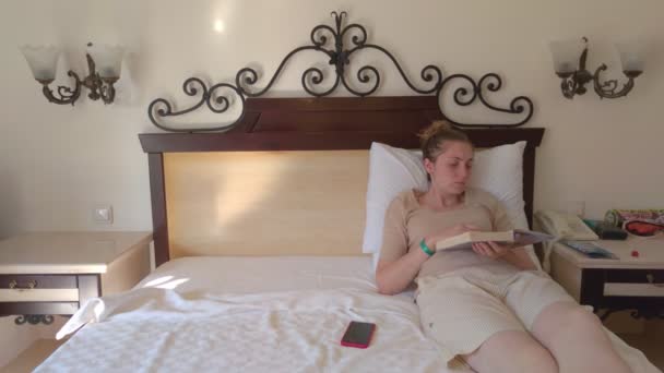Vrouw op bed leest een boek — Stockvideo