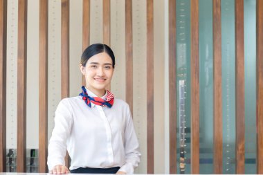 Gülümseyen genç bayan resepsiyonist işyerinde kameraya bakıyor. Otelde çalışan kadın resepsiyonistin portresi.