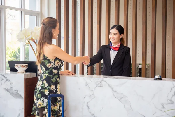 Otel resepsiyonunda el sıkışan mutlu resepsiyonist ve konuk, otel resepsiyonunda genç bayan yolcularla duran resepsiyonist