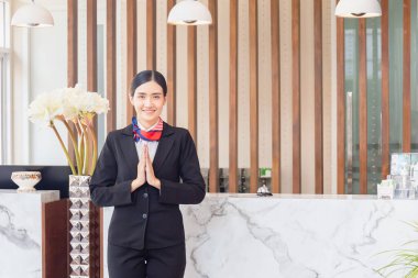 Resepsiyondaki Asyalı genç bayan resepsiyonist saygılarını sunuyor. Otelde çalışan gülümseyen kadın resepsiyonistin portresi.