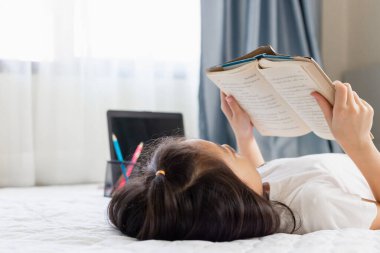 Yatakta kitap okuyan, gülümseyen mutlu ve rahat Asyalı bir çocuğun kitap, eğitim ve okul kavramlarını okuduğu seçici bir odak noktası.