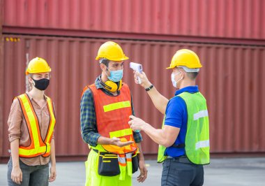 Kargo konteynerlerindeki Coronavirus (COVID-19) taraması ve korunması için ateşi dijital termometreyle kontrol eden fabrika işçisi