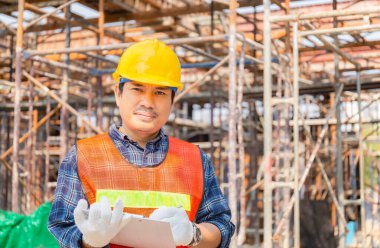 İnşaat alanında mühendis kontrol ve planlama projesi mavi arkaplan üzerinde pano kontrol listesi tutan adam.