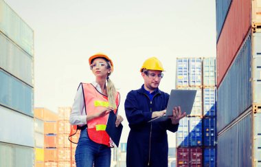 Pano kontrol listesi kullanan kadın ustabaşı yeleği ve kargodan konteynır yükleme kutusunu kontrol etmek için dizüstü bilgisayarlı işçi.