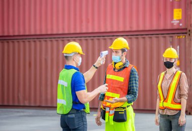 Kargo konteynerlerindeki Coronavirus (COVID-19) taraması ve korunması için ateşi dijital termometreyle kontrol eden fabrika işçisi