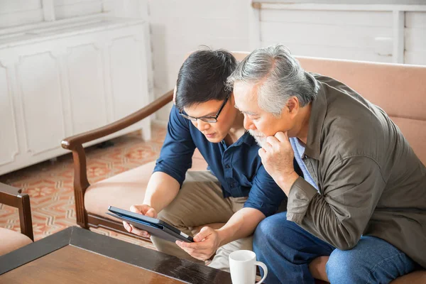 Cheerful senior asian father and adult son using tablet smartphone in living room, Happiness Asian family concepts