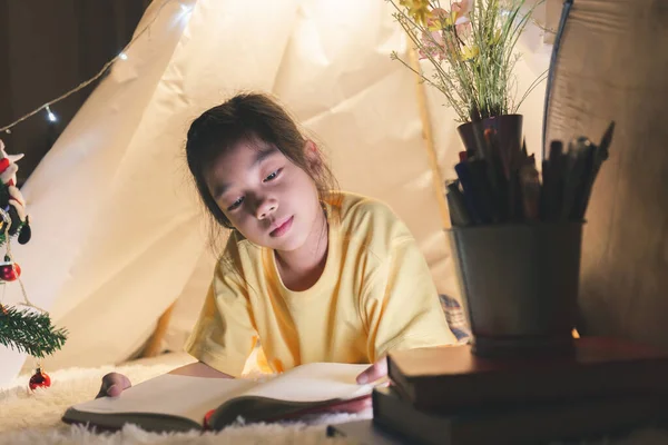 Little girl reading a book in tent, Happy kid playing at home, Funny lovely kid having fun in children room.