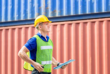 Pano kontrol listesi tutan fabrika işçisi kargo kutusundaki kutuları kontrol ediyor.