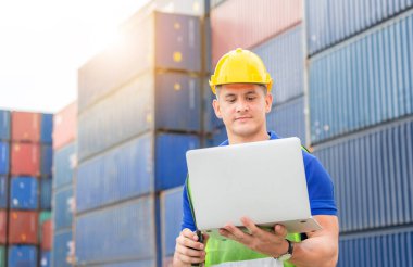 Kask ve güvenlik yeleği giyen mühendis elinde dizüstü bilgisayar ve çift yönlü telsiz, Foreman işçi kontrolü kargo kutusundan konteynerleri yüklüyor.
