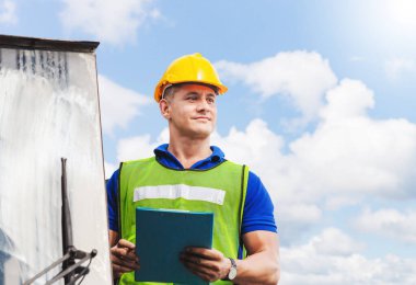 Kask ve güvenlik yeleği giymiş işçiler konteyner stackers üzerinde duruyor. Yükleme konteynerlerini kargo kutusundan kontrol ediyorlar.