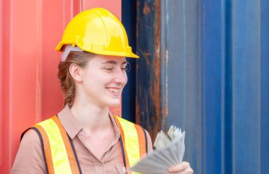 Neşeli genç bayan işçi, rahatlamak ve konteynır kargosunda para banknotları tutarak oturuyor.