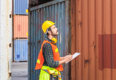 İşçi pano kontrol listesi tutuyor ve kargodan konteynır kutusunu kontrol ediyor