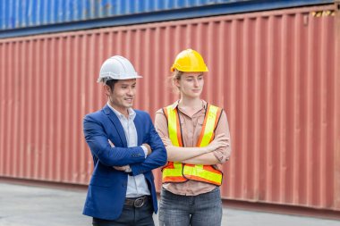 Kasketli neşeli fabrika işçisi takımı kargo konteynırlarında kolları bağlı gülümsüyor.