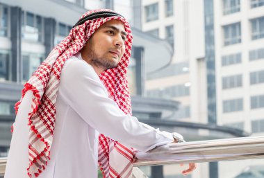 Ayakta duran genç Arap Orta Doğulu adamın portresi şehir manzarası arka planında eğleniyor.