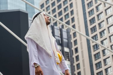 Orta Doğulu genç bir Arap 'ın portresi gökyüzüne bakıyor, Müslüman mühendis şehir merkezinde yürüyor.