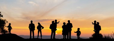 Aile dağda günbatımının tadını çıkarıyor. Tepedeki büyükanne ve torunun silueti ve gün batımını izlemek, Mutlu aile kavramı.