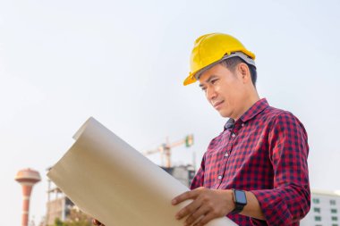 Mühendis kontrol ve planlama projesi inşaat alanının planlarını elinde tutan kasklı adam.