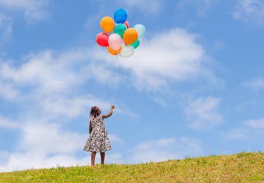 Kesme yolu olan küçük kız balonlarla oynuyor, mavi gökyüzü arka planında hava topları tutan Afrikalı Amerikalı kız.