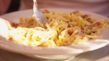 Sokak kafesi, bir adam kaşıkla bir çatala sarılmış, güneş ışığında beyaz bir tabakta spagetti Carbonara