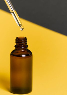 Seçici odaklanma. Pipetli cam bir kavanoz. İçinde yüz ve vücut için kozmetik bir organik yağ var. Sarı-gri kağıt arka planda. kopyalama alanı