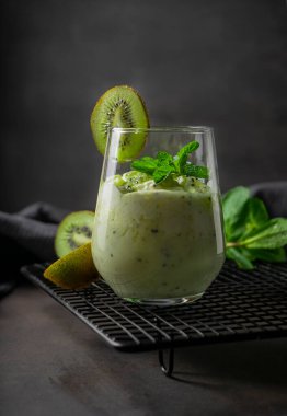 Olgun kividen yapılmış tropik meyve püresi. Düzgün beslenme, düşük kalorili sağlıklı meyve suyu. Nane filizli karanlık bir arka planda