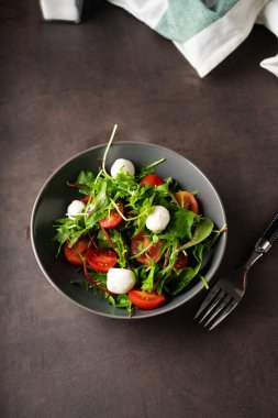Hafif atıştırmalık Marul yapraklı taze yeşil salata ve roka yeşili. Çeri domatesli ve mozzarella peynirli. Gösterişsiz, karanlık ruh hali, kopyalama alanı. yemek tarifli menüler ve dergiler için