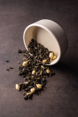 Seçici odak, yasemin çiçekli doğal siyah yaprak çayı. Kil kasesinde demleniyor. Dikey açı, makro. Karanlık bir arka planda. Menüler ve kafeler için