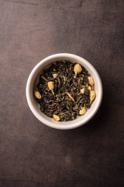 Seçici odak, yasemin çiçekli doğal siyah yaprak çayı. Kil kasesinde demleniyor. Dikey açı, makro. Karanlık bir arka planda. Menüler ve kafeler için