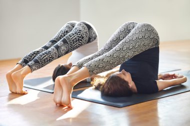 Yoga asana yaparken iki genç kadın poz pulluk