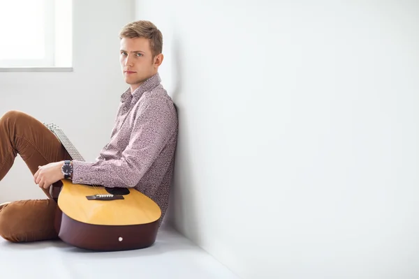 Knappe man met gitaar aanbrengen op de vloer — Stockfoto