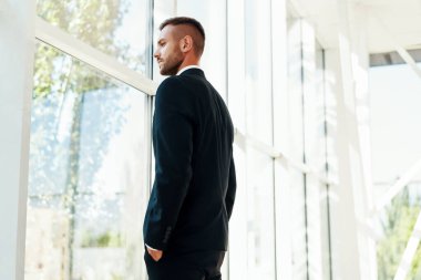 Modern yaratıcı ofisin zarif süitinde panoramik pencerelere bakan kendine güvenen iş adamı.