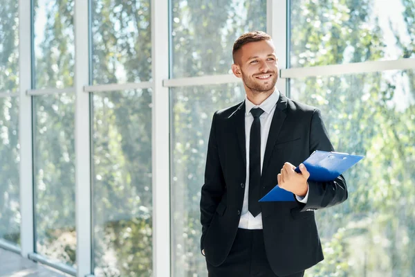 Knappe lachende zakenman met klembord in een licht modern kantoor — Stockfoto
