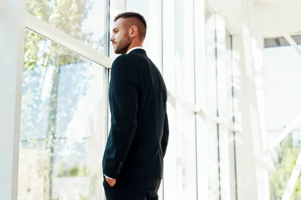 Hombre de negocios seguro en suite elegante en la oficina creativa moderna que mira en ventanas panorámicas — Foto de Stock