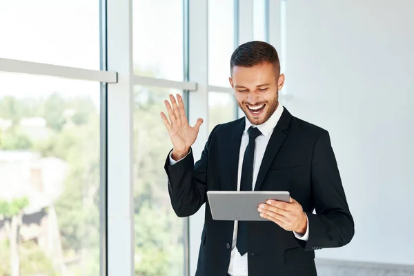 Gelukkige succesvolle zakenman in elegante suite lezen goed nieuws met behulp van tablet in moderne creatieve kantoor achtergrond — Stockfoto