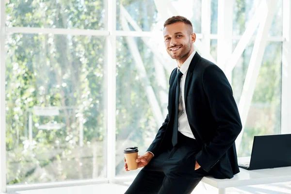 Gelukkig knappe zakenman ontspannen met een kopje koffie in de hand tijdens de pauze in modern kantoor met kopieerruimte — Stockfoto