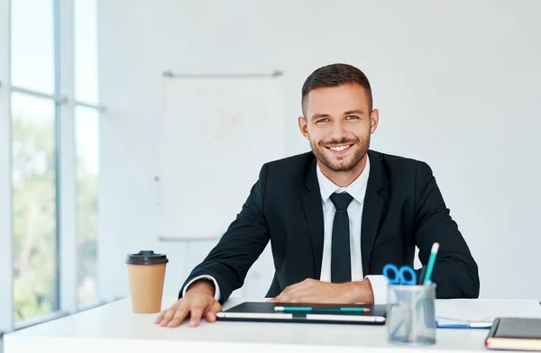 Un om de afaceri elegant zâmbitor în costum elegant care stă la biroul său într-un birou modern luminos — Fotografie, imagine de stoc