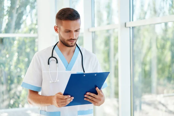 Portrait of confident male doctor with stethoscope and clipboard in medical uniform — Stock Photo, Image