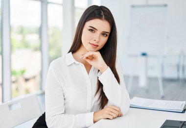 Modern ofisteki masada oturan ve kameraya bakan gülümseyen genç iş kadınının portresi.